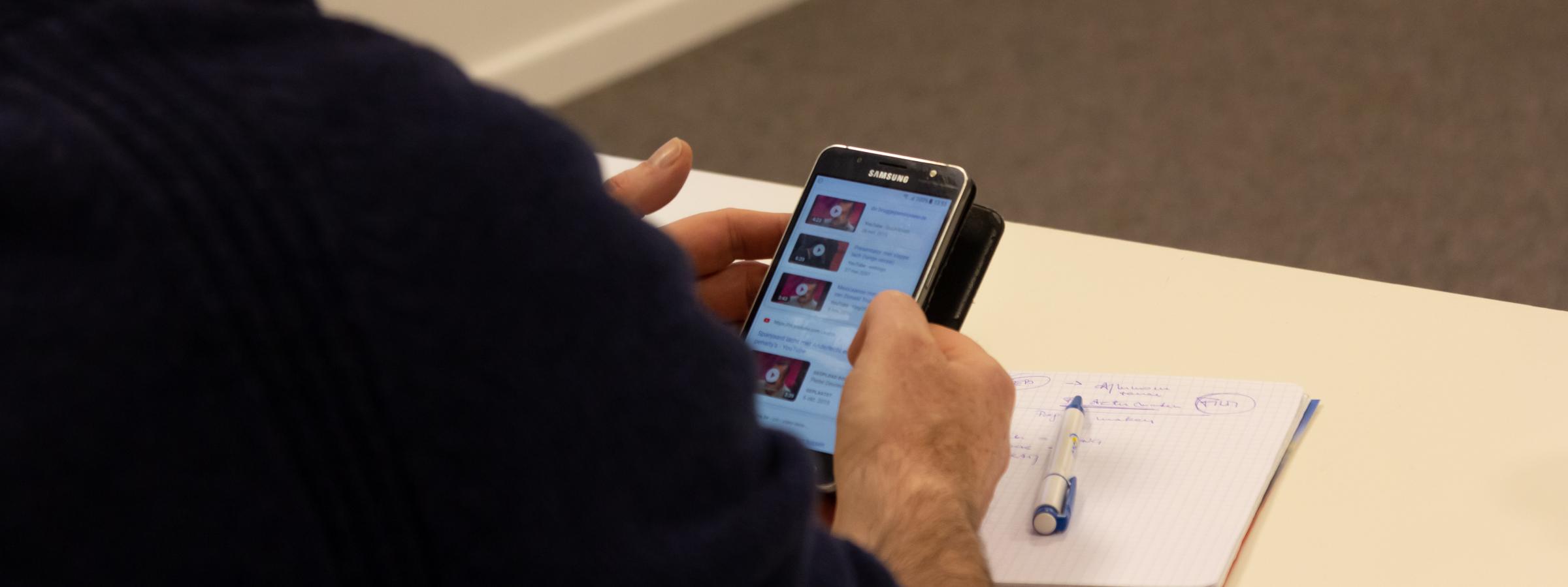 Persoon op smartphone tijdens vergadering