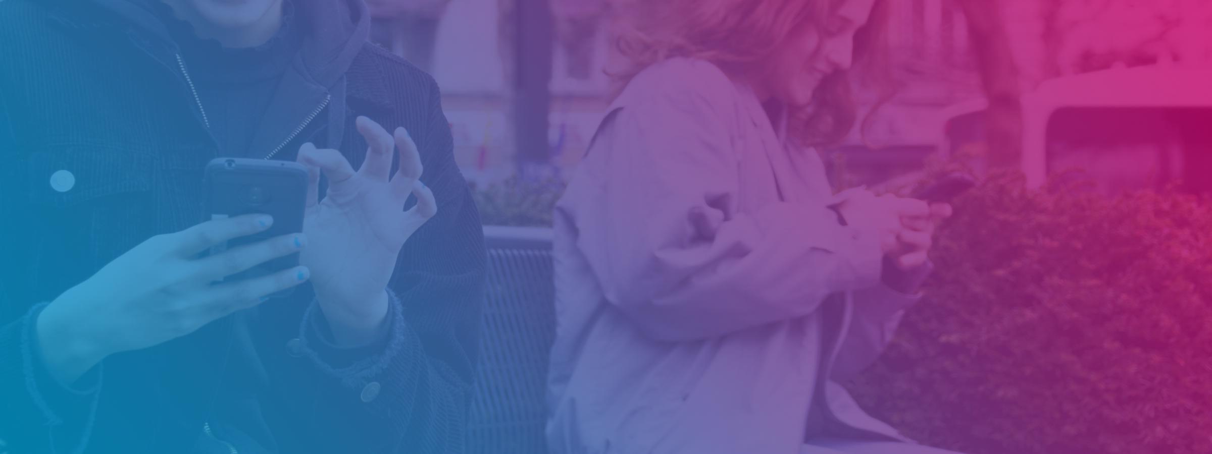 Twee meisjes zitten op een bankje, allebei met hun smartphone