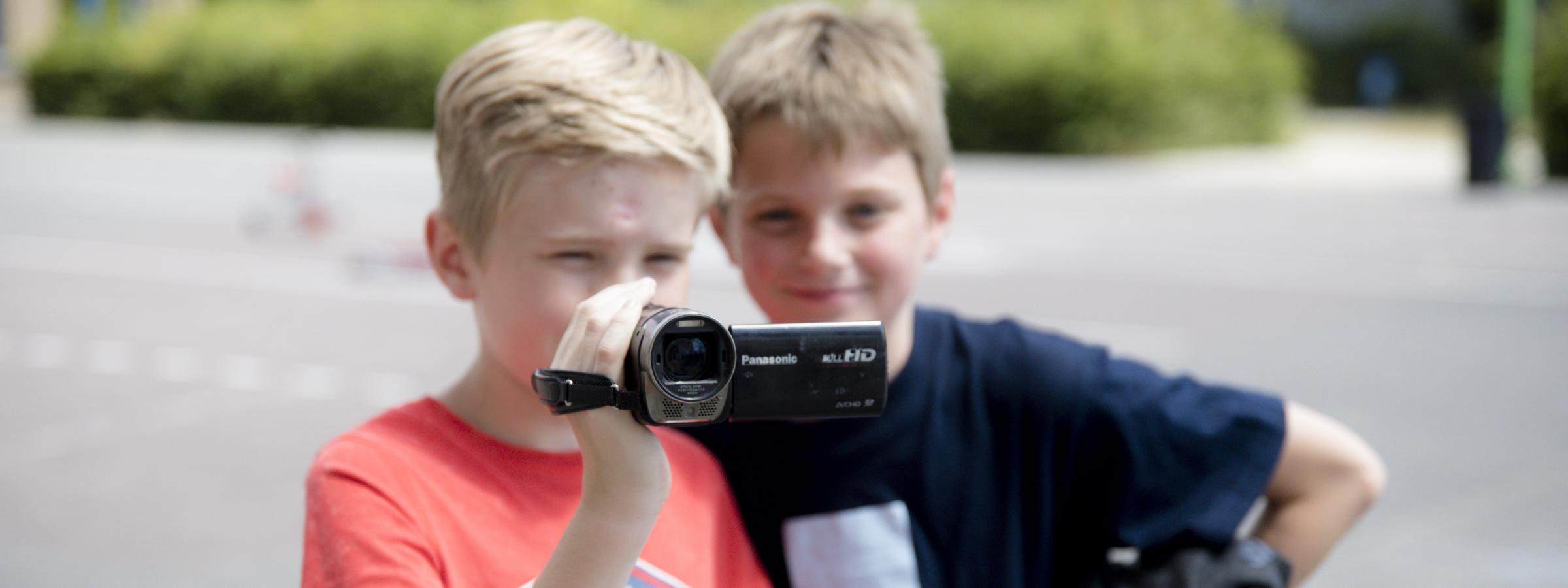 Jongen met camera vast, jongen achter hem kijkt mee wat hij filmt