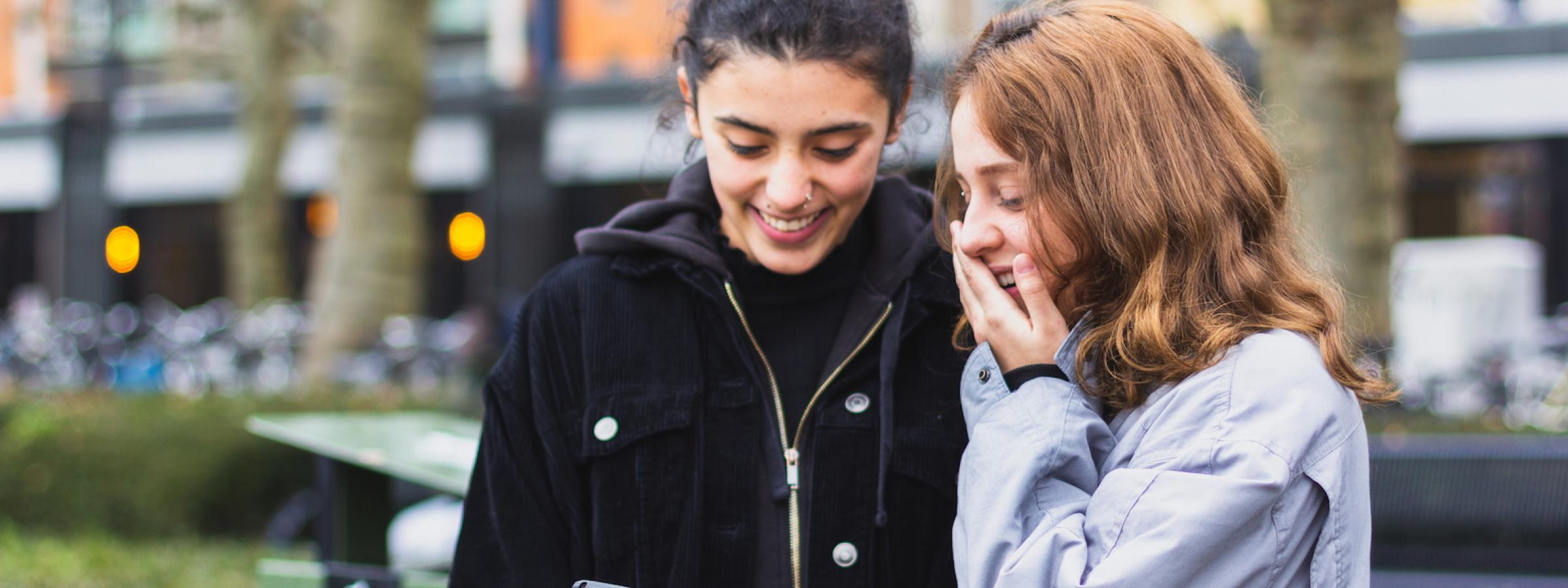 Meisje toont iets op haar smartphone aan ander meisje, ze lachen