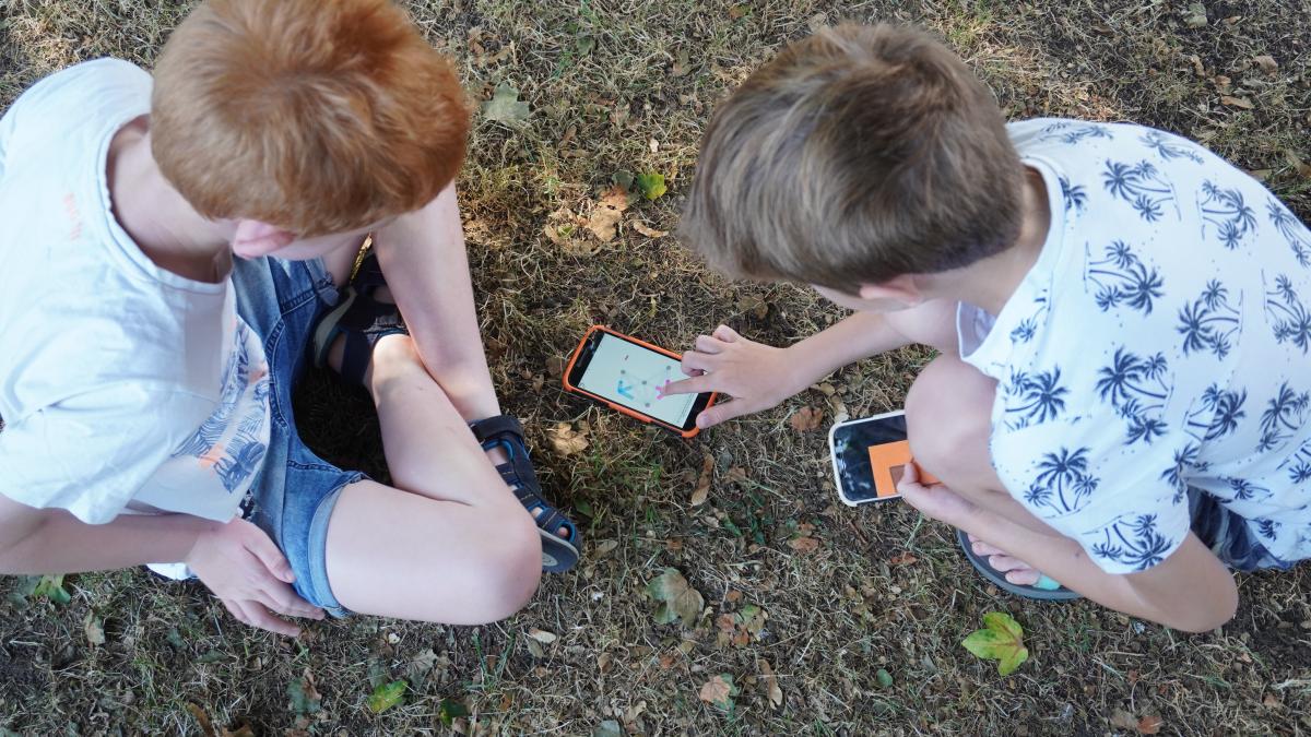Twee jongens in het zand, eentje raakt het scherm van een smartphone aan